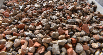 Nahaufnahme von kleinen, unregelmäßig geformten Steinen und Ziegelstücken in verschiedenen Grau- und Rottönen. Die Steine liegen locker geschichtet und wirken wie sortiertes Recyclingmaterial oder Zuschlagstoffe für die Betonherstellung.

                                    